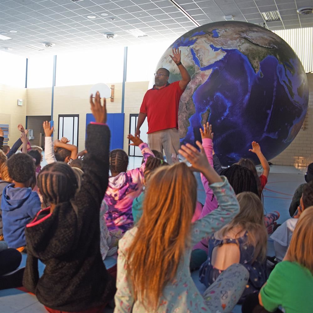  inflatable earth in background of students raising hands