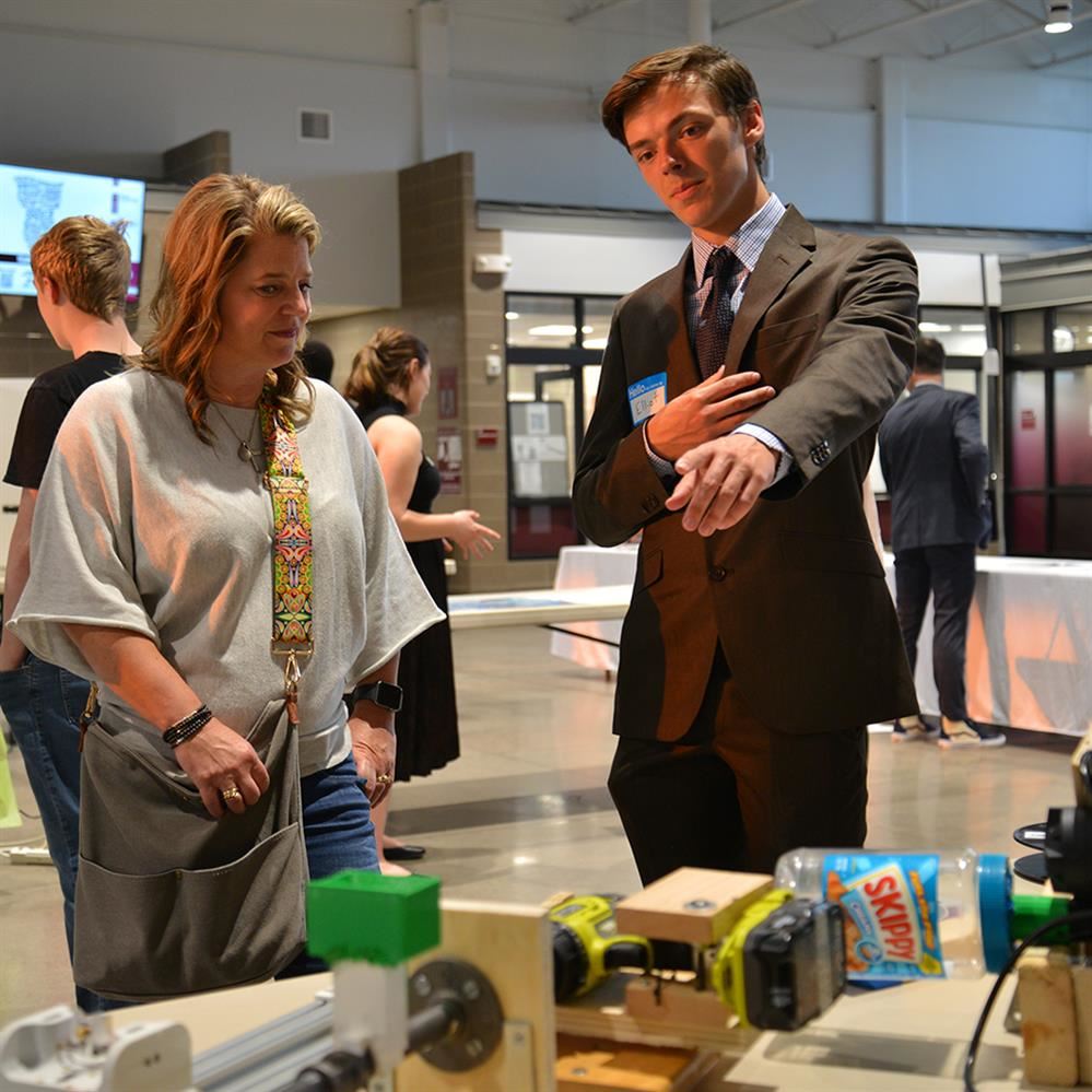  student talking and pointing to project on a table 