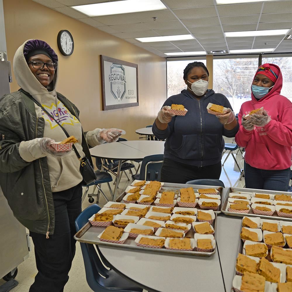  three students smiling and holding pumpkin bars