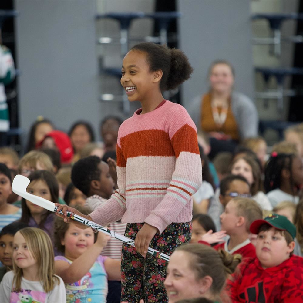 student smiling holding a floor hockey stick 