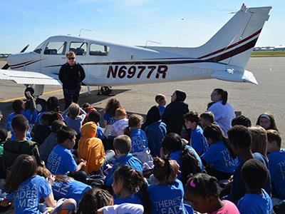 students looking at pilot with an airplane in the background