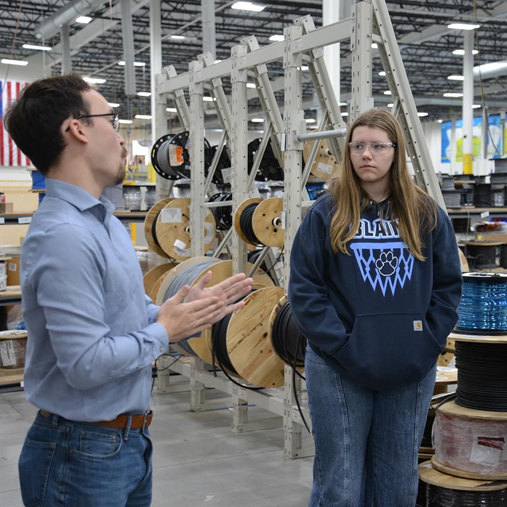  student listening to tour guide with spools of wire behind them