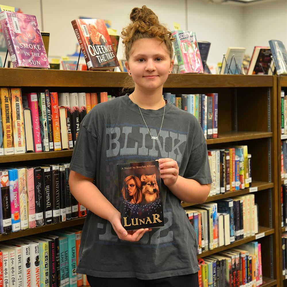  Braylan holding her book in a library 