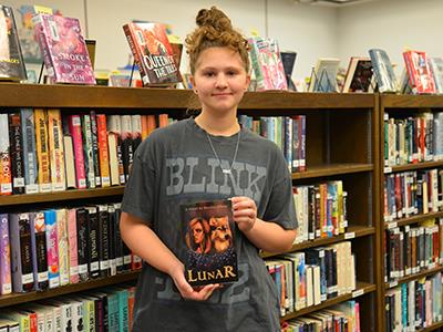 Braylan holding her book in a library