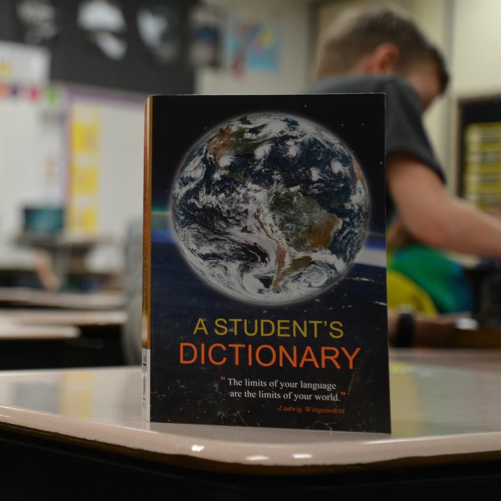 Dictionary on a desk with students in the background 