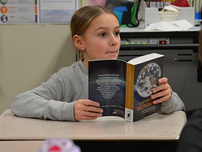 student at her desk holding open a dictionary 