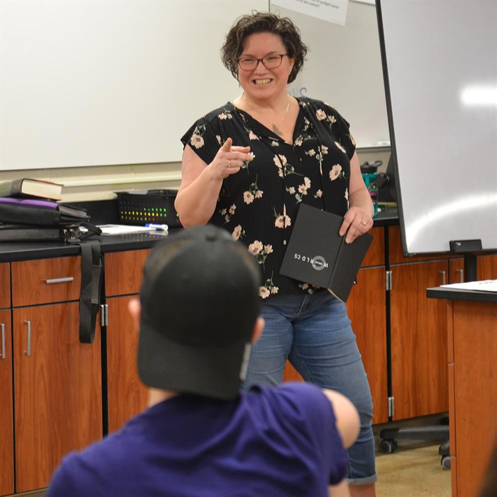  Erin at the front of a classroom smiling and pointing to a student
