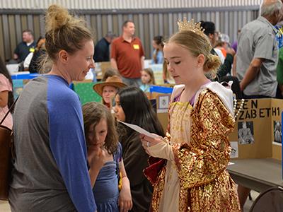 student dressed as Queen Elizabeth reading off a paper to an adult