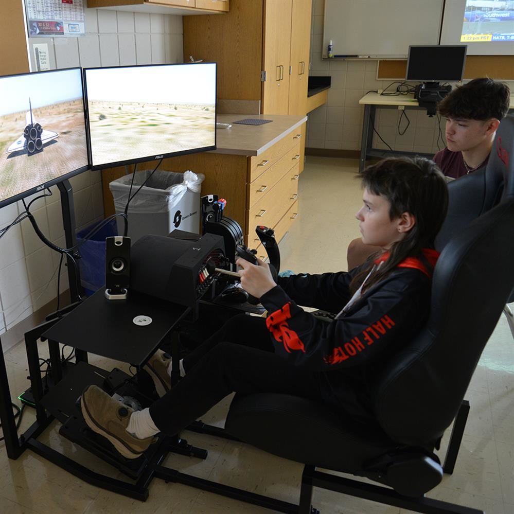  elementary student on the simulator with high school student watching