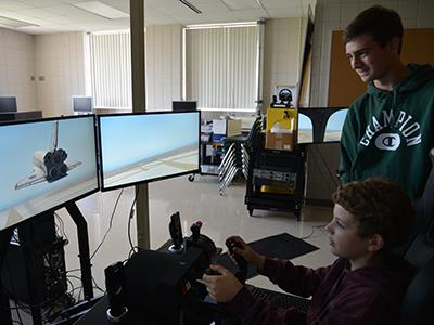 high school student overlooking elementary student on a flight simulator