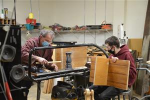 an instructor and student do woodworking in a shop 