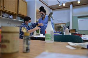 instructor and student painting a piece of wood 