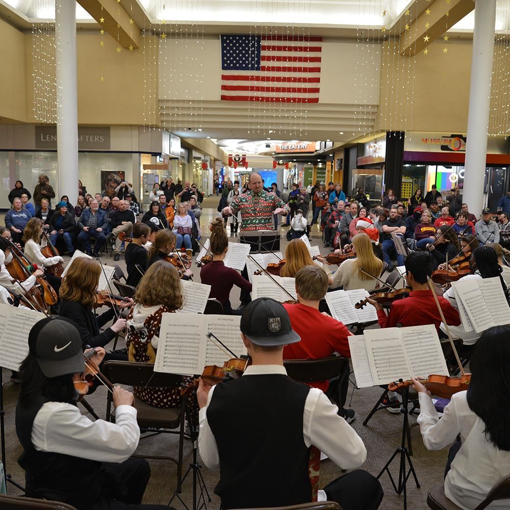  orchestra students playing at a mall with patrons looking on