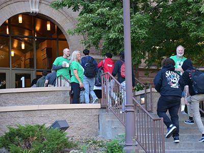 students walking up the steps to the front of the building with smiling administrators 
