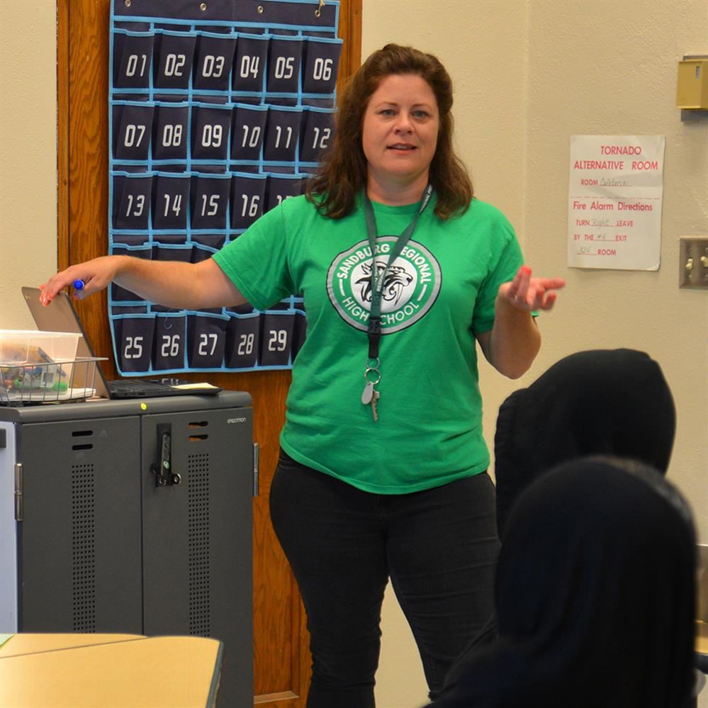  teacher in front of room with t-shirt with the new Saber logo