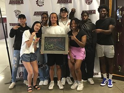 8 students gathered with Anoka HS backdrop behind them