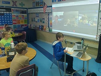 student at computer with projector behind him with Zoom call