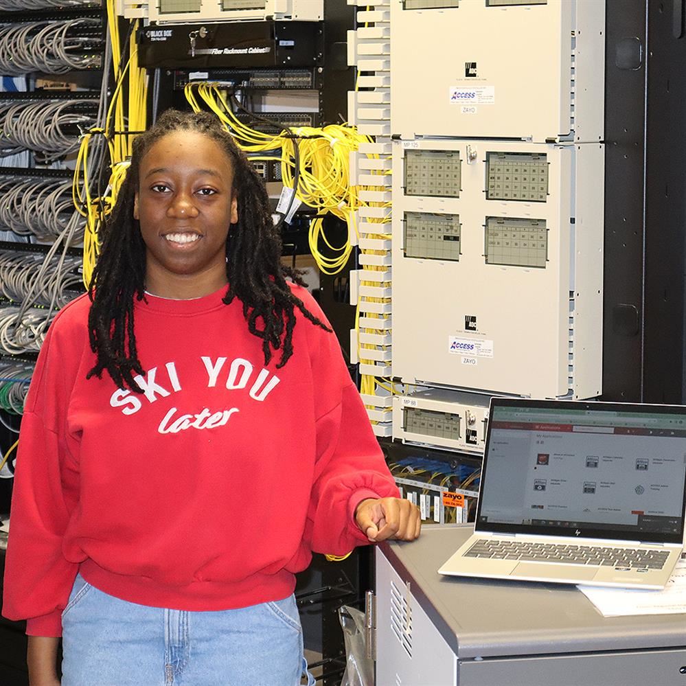  Mya Benson standing next to a laptop computer in a network room